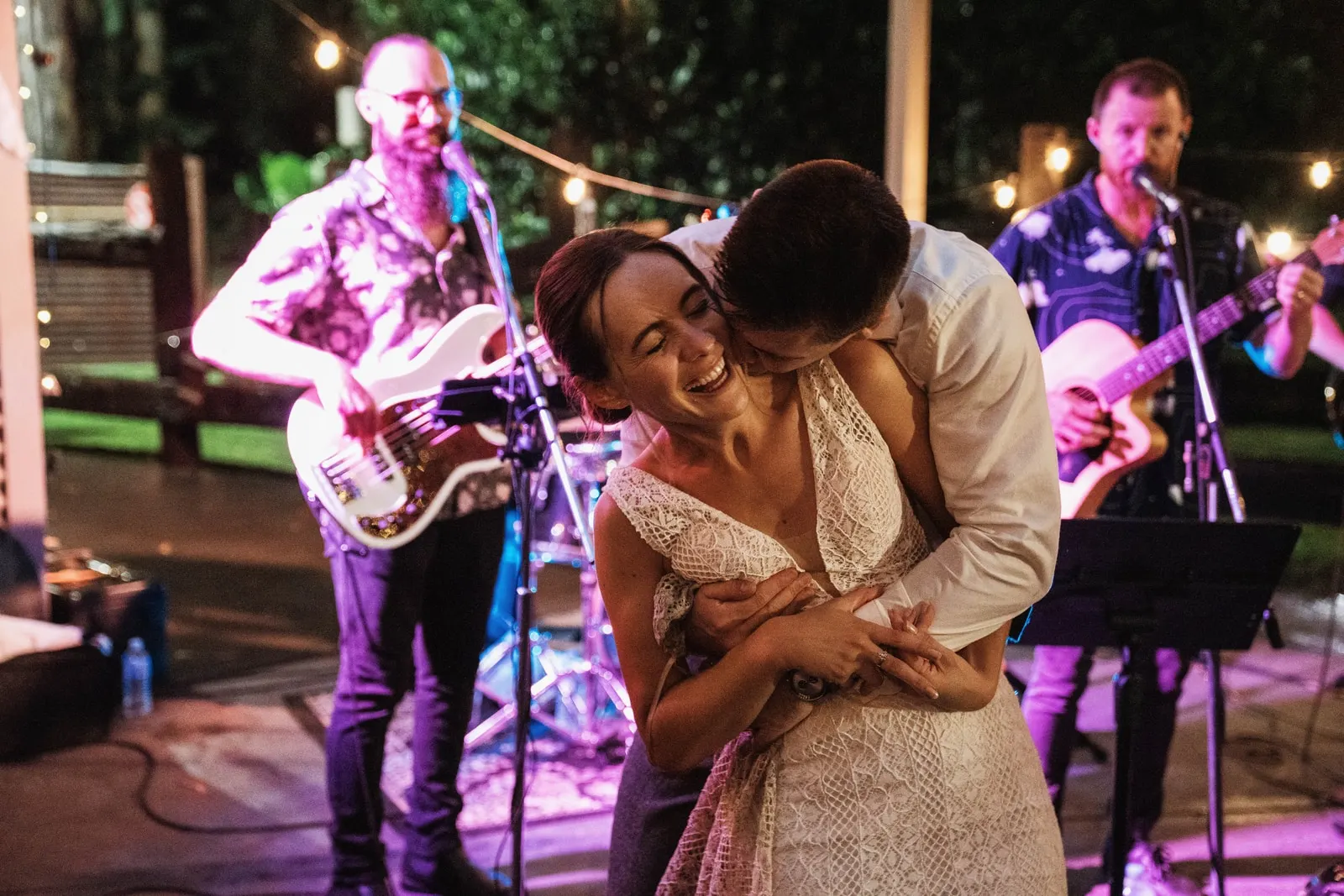 Newlyweds dancing in front of a live band at an outdoor evening reception